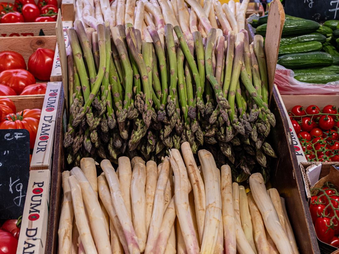 Bundles of green and white asparagus stacked on a French market stall.