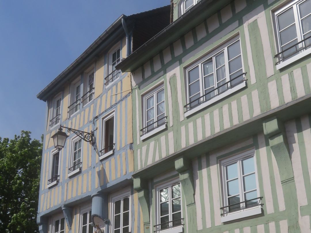 A row of timber-framed houses on the rue Guynemer at Elbeuf, painted green and cream, the framing running the full height of the facade.