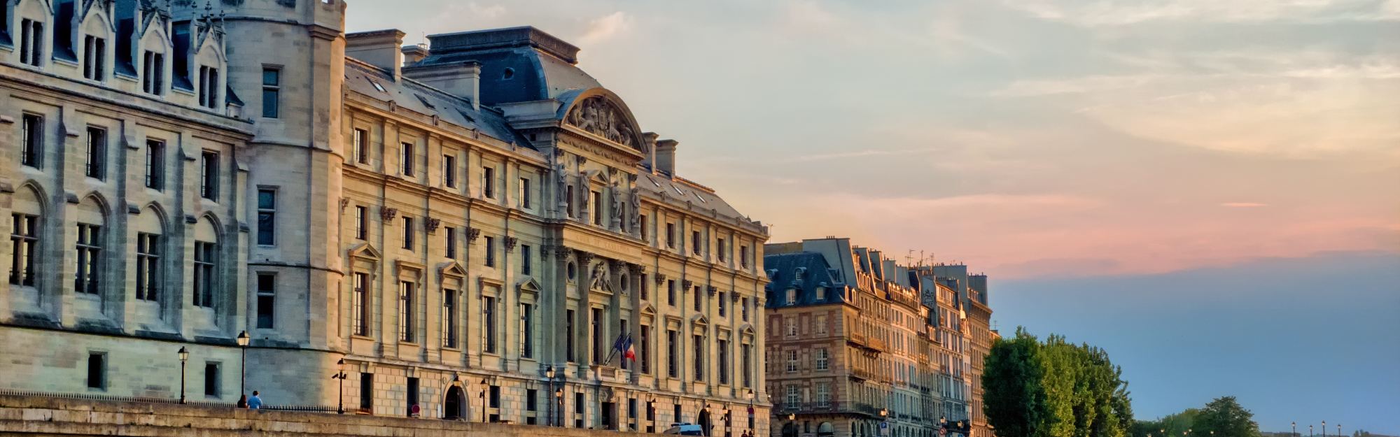 The Seine at dusk in Paris, the arches of the Pont Neuf and the long stone frontage of the Île de la Cité under a pink sky.